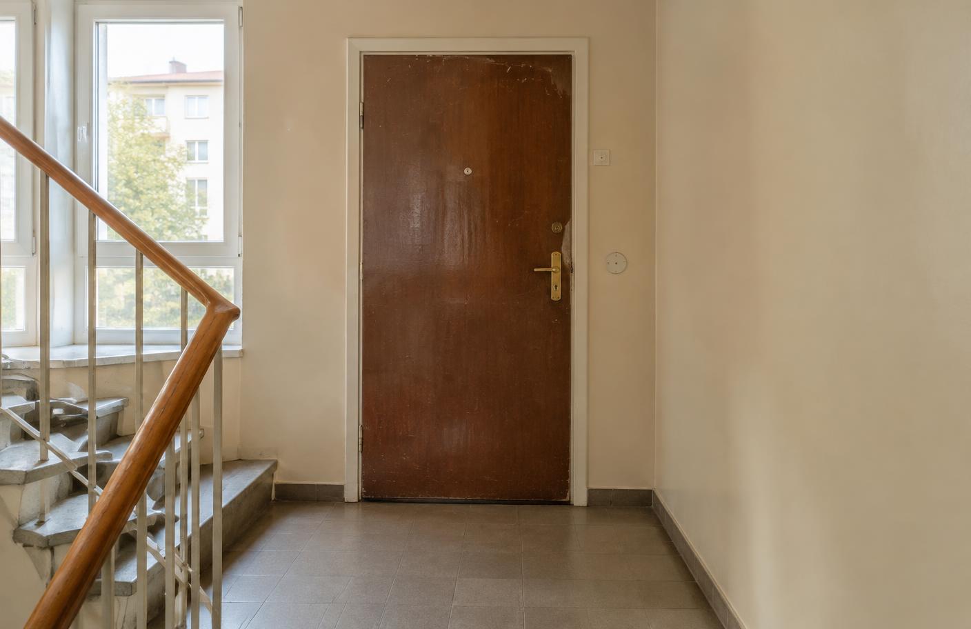 Sliten innerdörr i mörkbrunt laminat i ett trapphus, före foliering